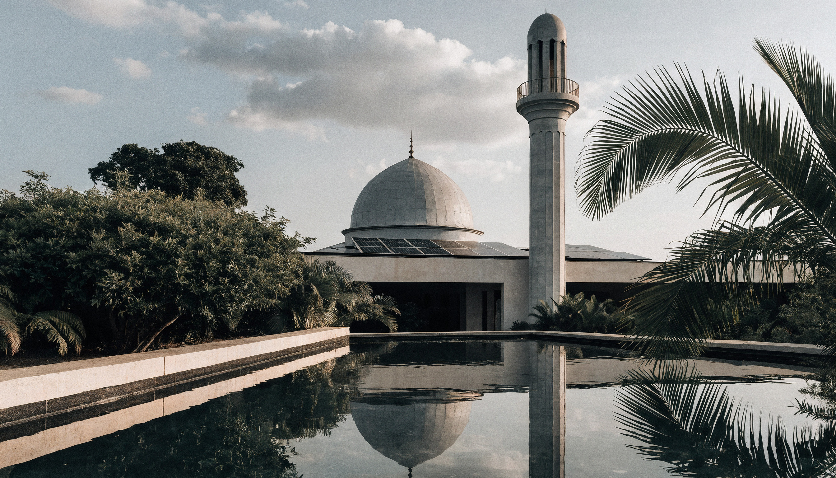 Çatısında güneş panelleri olan modern bir cami ve önündeki yansıtıcı havuz