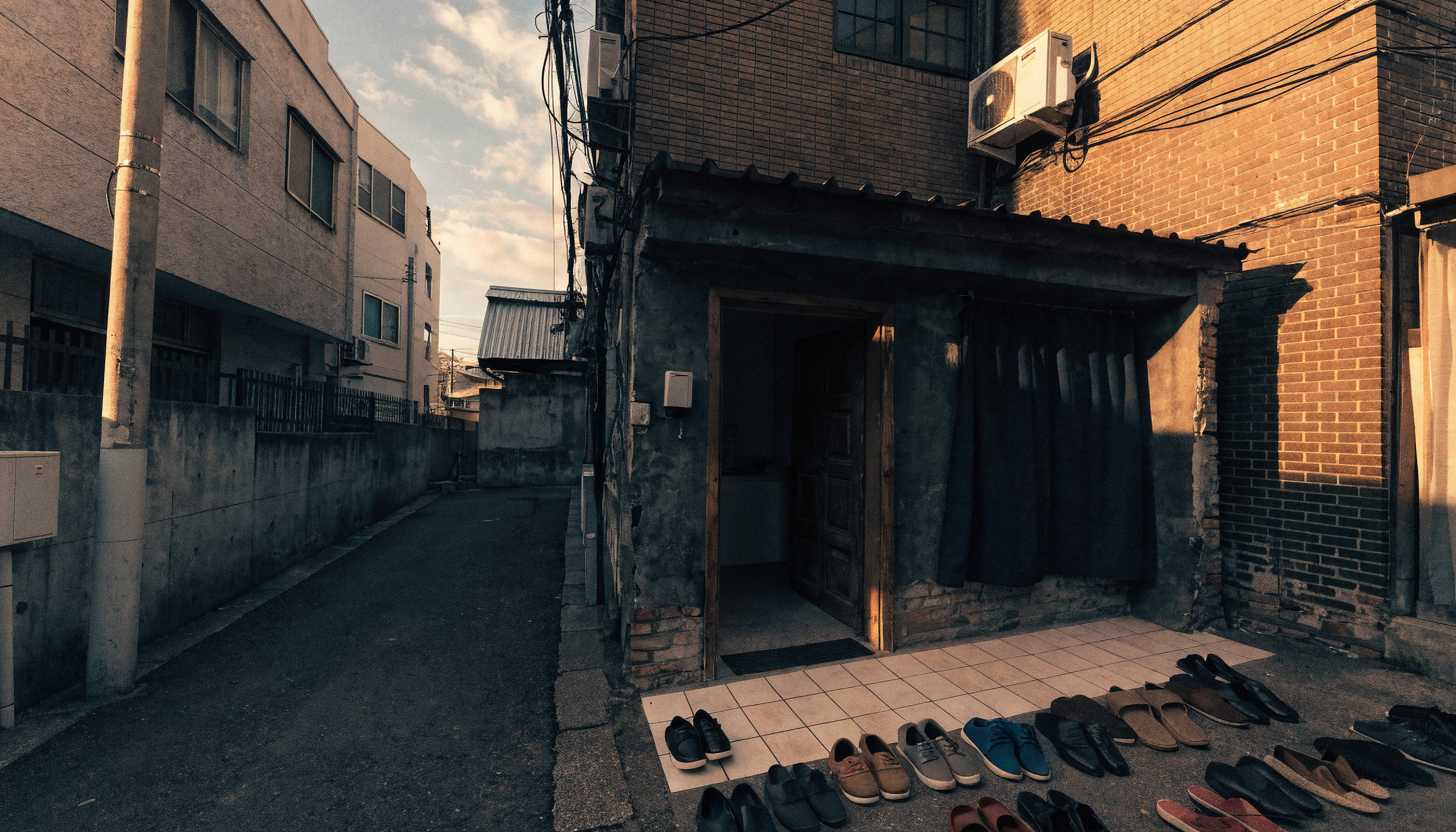 Osaka'nın dar bir sokağında akşam ışığında bir mescit girişi ve önünde dizili ayakkabılar